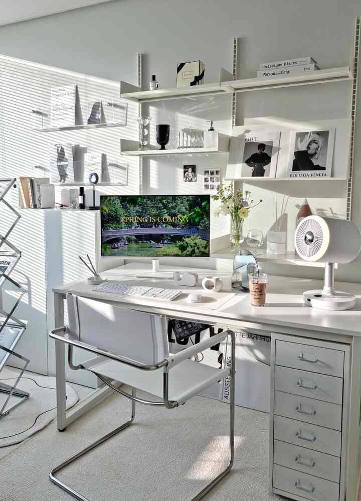 Bright white-toned studio home office featuring Mid-Century Modern chair, shelves, desk with computer, and a circulator fan in a clean space