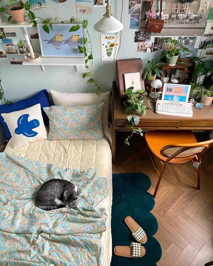 白と茶色のトーンでまとめられたコンパクトなホームオフィス、ベッドとデスクが配置され、植物が彩る落ち着いたインテリア