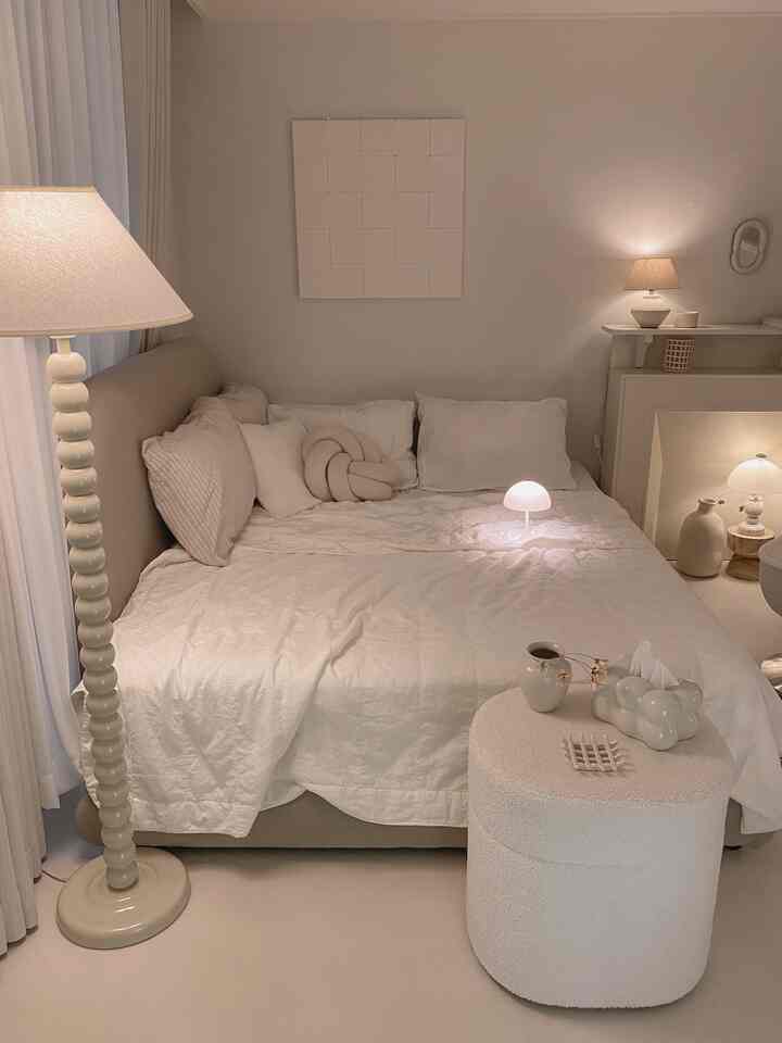 暖かいベージュとアイボリーの色調の寝室、ベッドとスツール、照明が心地よく配置されたモダンな雰囲気のインテリア