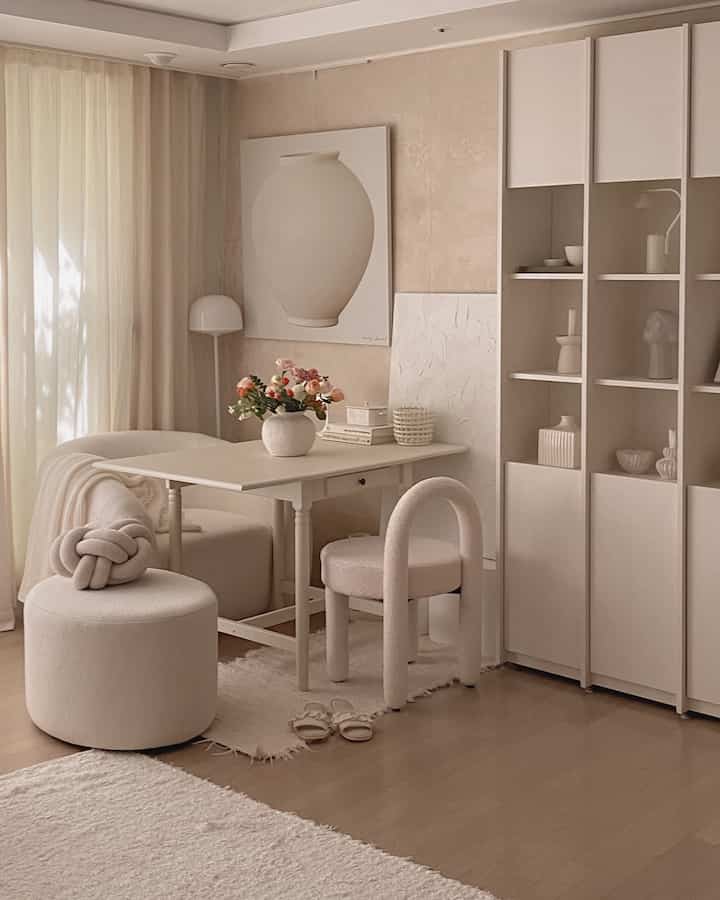 アイボリーとベージュのトーンが漂うリビングのおうちカフェ空間、折りたたみテーブルと個性的なアーチ型チェア、スツール、カーテンが配置された雰囲気のあるインテリア