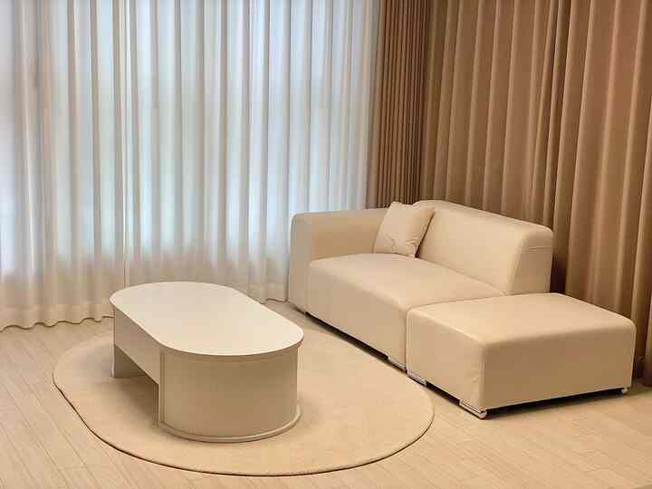 Beige and white toned living room featuring a simple beige sofa and white coffee table on a round rug, creating a cozy atmosphere