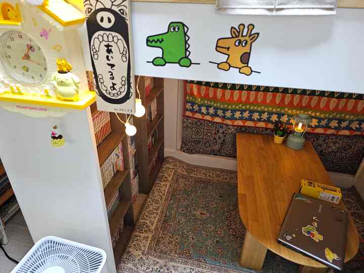 ナチュラルな色調の小さな空間、本棚と木製テーブル、多彩なラグが配置された雰囲気のある読書とくつろぎのインテリア