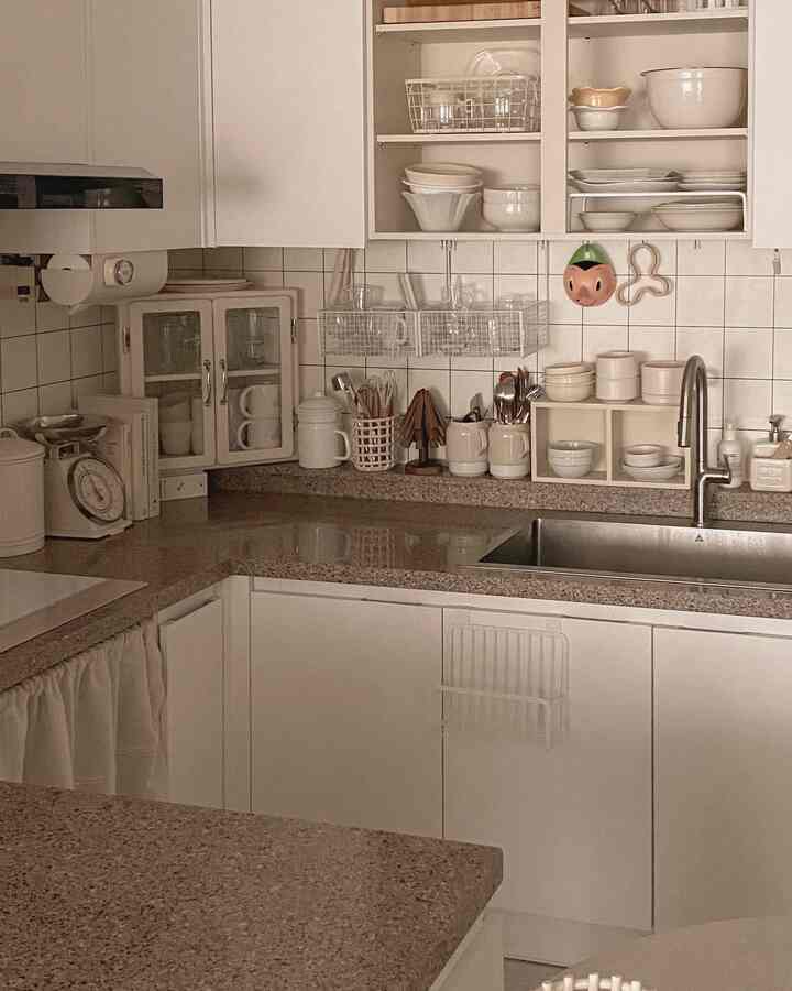 柔らかなホワイトとブラウンのトーンのキッチン、整然とした収納棚と壁に掛けられたアレッシィのピノキオじょうごがある雰囲気のある空間