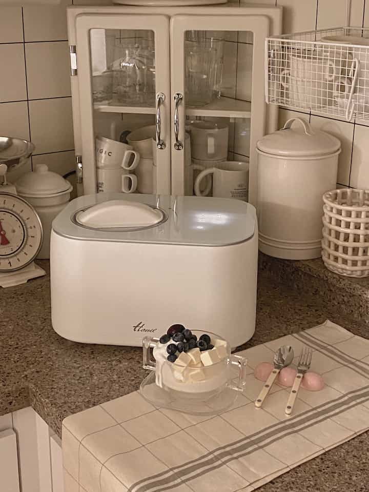 暖かみのあるクリーム色とナチュラルブラウンのキッチン、整頓された収納棚と小型家電が配置された雰囲気のあるインテリア