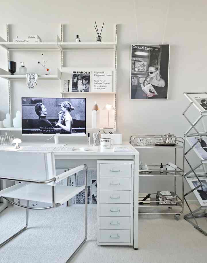Clean mid-century modern home office space dominated by white and monotone tones featuring desk, trolley, and wall shelves harmoniously arranged