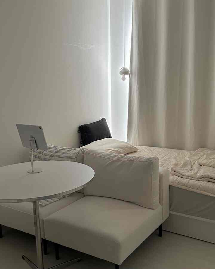White and beige toned studio bedroom featuring a sofa and bed arranged for efficient use of space in a cozy setting