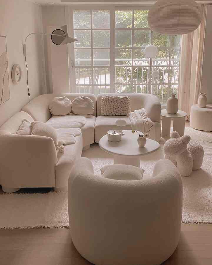 ホワイトとナチュラルカラーの調和がとれたリビング、広いコーナーソファと丸いコーヒーテーブルが居心地の良い空間を作る