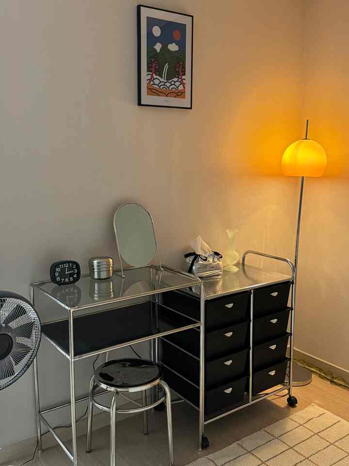 ベージュの壁とライトウッドの床で構成されたナチュラルモダンなパウダールーム、シルバーの金属フレームの化粧台とブラックの収納が配置された空間