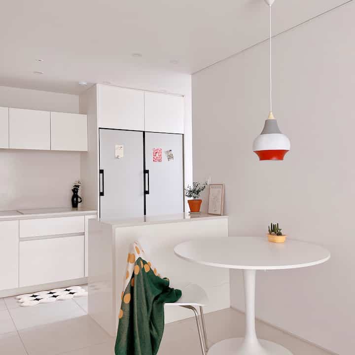白を基調としたキッチンスペース、ラウンドテーブルとカラフルなスロー、特徴的なペンダントライトが配置された洗練されたモダンインテリア