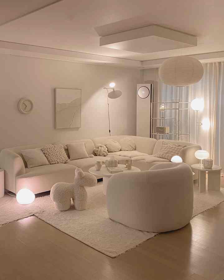 柔らかなホワイトとベージュトーンのリビング、広いモジュラーソファと照明、サイドテーブルが快適な雰囲気を演出する空間