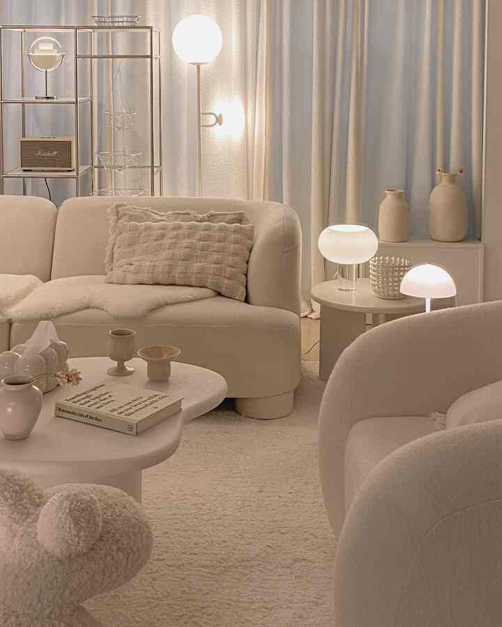 ベージュとホワイトの色調のリビング、曲線のソファとアームチェア、照明が配置された柔らかく自然な雰囲気のあるインテリア