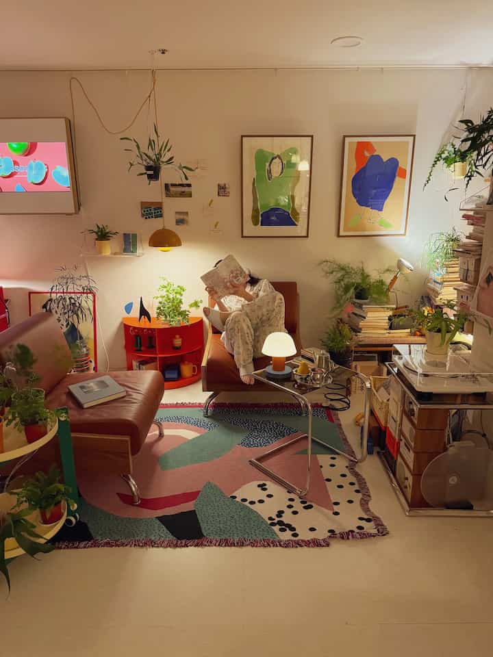 Mid-century modern studio study featuring brown leather chairs, abundant plants, and yellow pendant lighting creating a cozy atmosphere