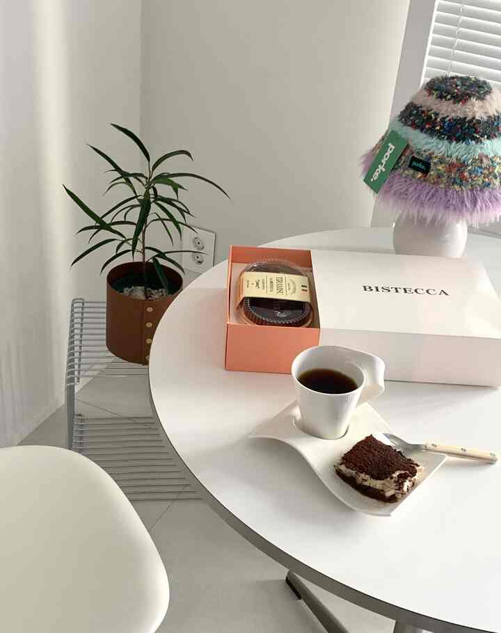 White-toned dining room featuring round table, coffee mug, and tiramisu, creating a simple and modern atmosphere