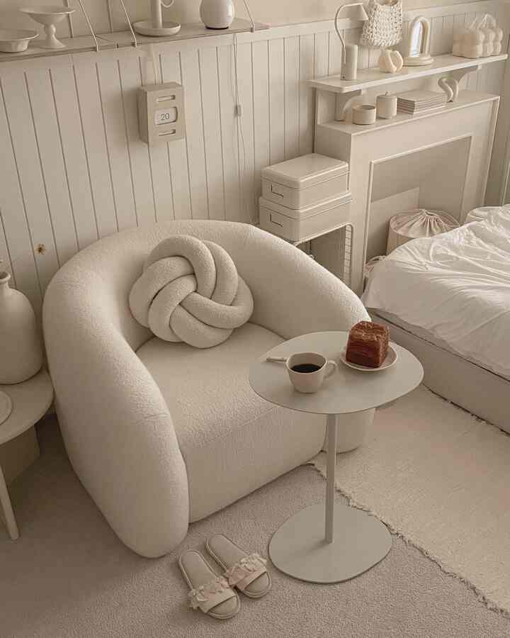 温かみのあるナチュラルカラーの小さなリビング、柔らかな曲線のアームチェアとサイドテーブル、シンプルで居心地のよいインテリア