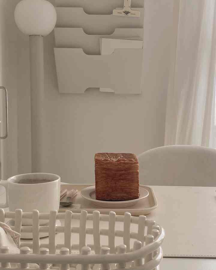 柔らかなホワイトトーンのダイニング空間、清潔感のあるテーブルにコーヒーとベーカリーが置かれたシンプルなインテリア