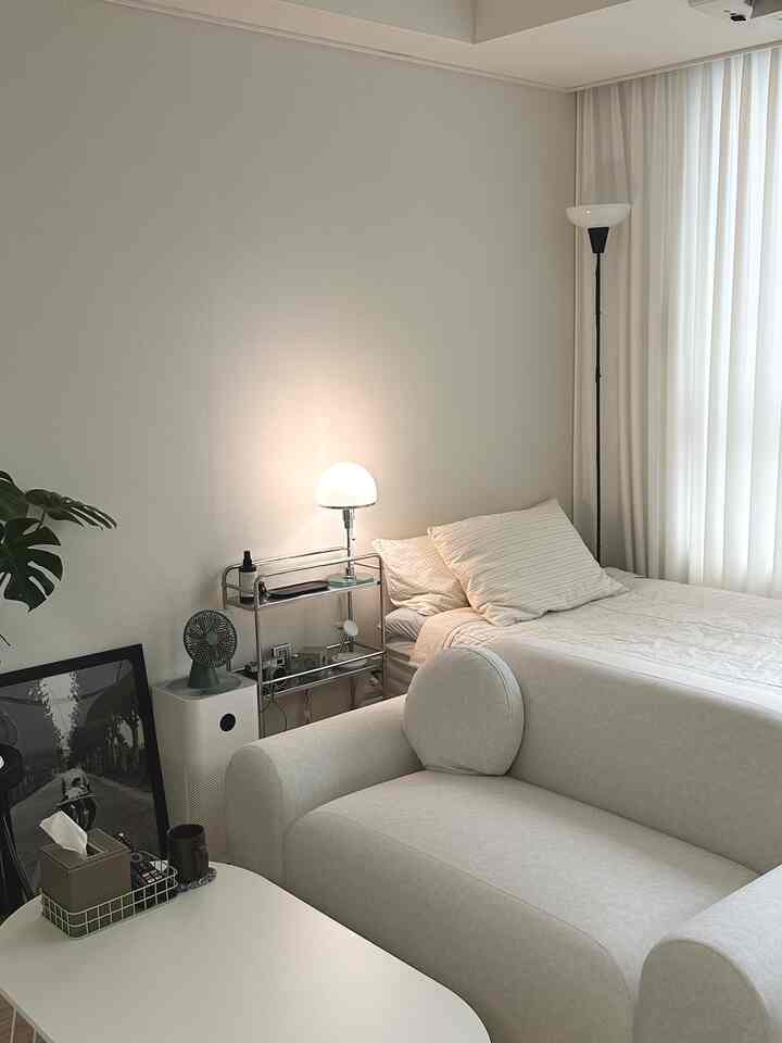 Natural beige and white-toned studio bedroom featuring a sofa, bed, and warm lamps creating a cozy modern atmosphere