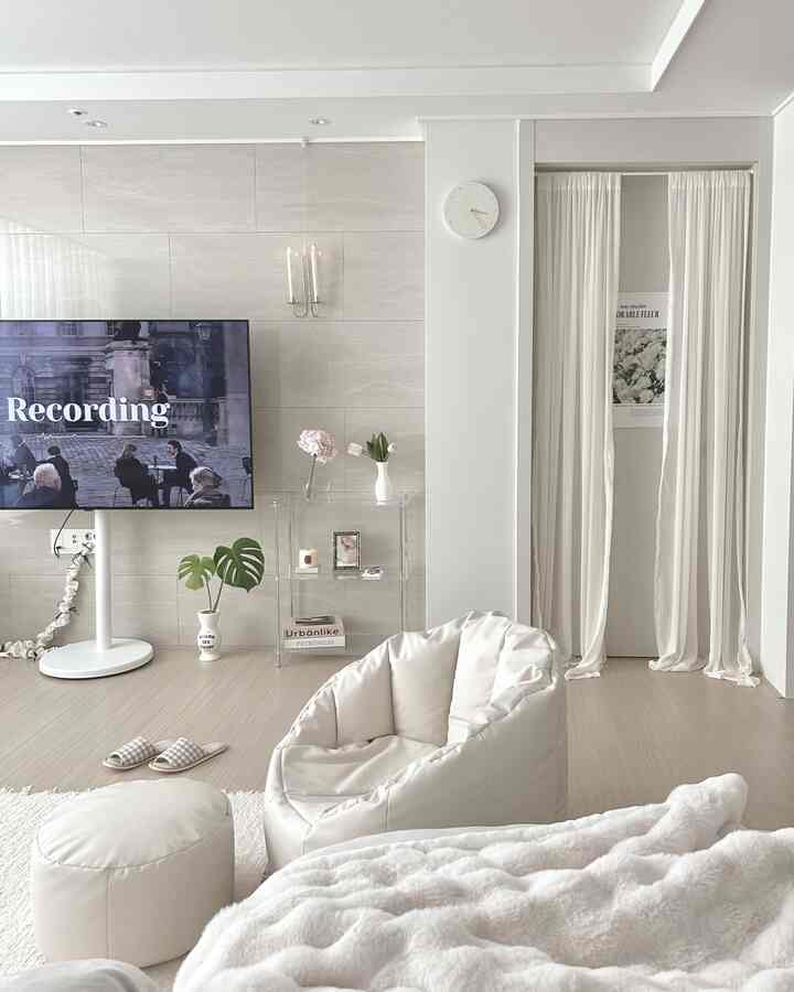 明るいホワイトとシルバーの色調のリビング、中央にベージュのビーズクッションと白いスロー、透明なアクリル棚が配置されたモダンなインテリア