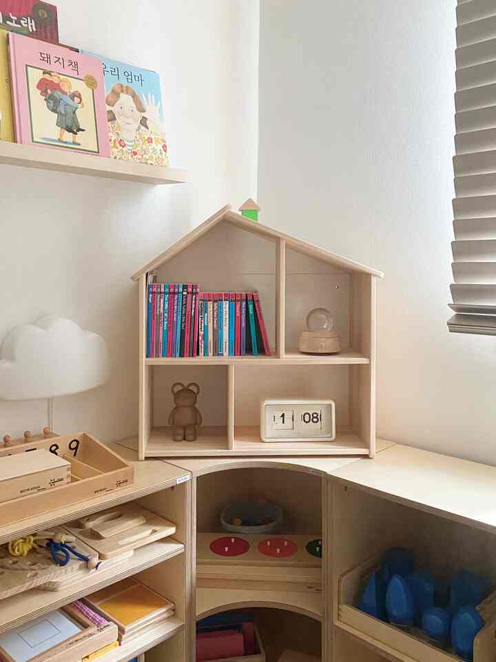 明るい木目調の子供部屋、ドールハウス型の本棚と赤ちゃん向けの小物、ムードライトが置かれた雰囲気のあるインテリア