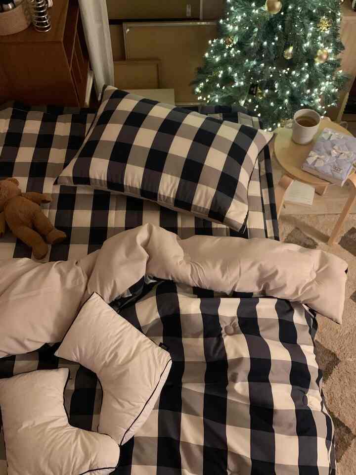 ネイビーとベージュのチェック柄寝具、小さな木製スツール、灯りのともったクリスマスツリーが配置された居心地の良いリビング