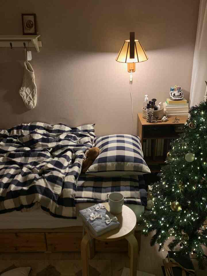 暖かいベージュとネイビーのチェック柄が特徴の寝室、居心地の良い照明とクリスマスツリーが配置された印象的な空間