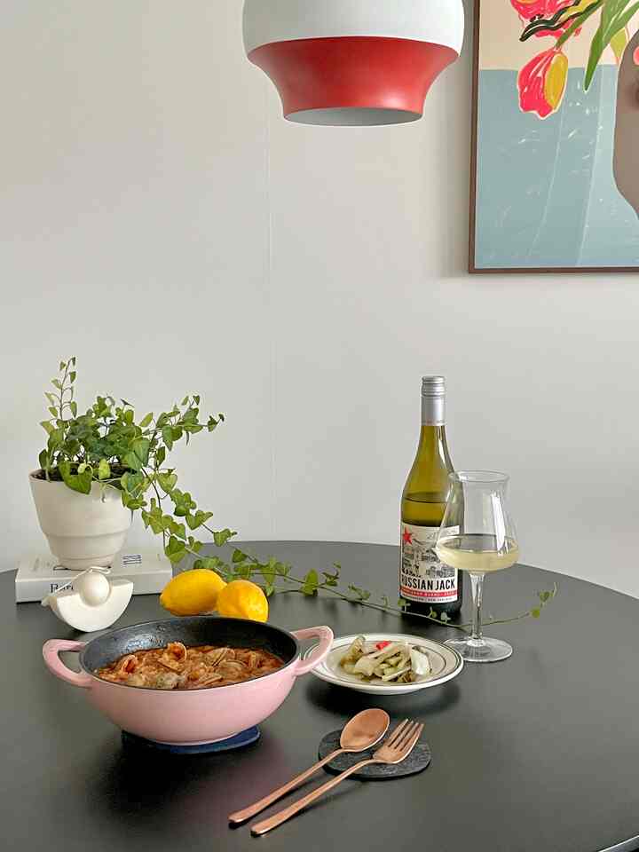 ブラックのラウンドテーブルにピンクの鍋、ワインボトルとグラス、カトラリー、植物が配置された温かみのあるホームカフェのインテリア