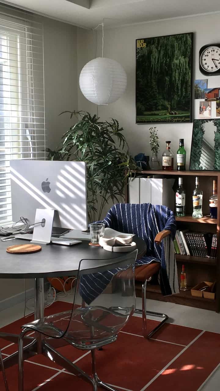 A natural modern home office with bright orange rug, transparent chair, and a desk featuring a computer