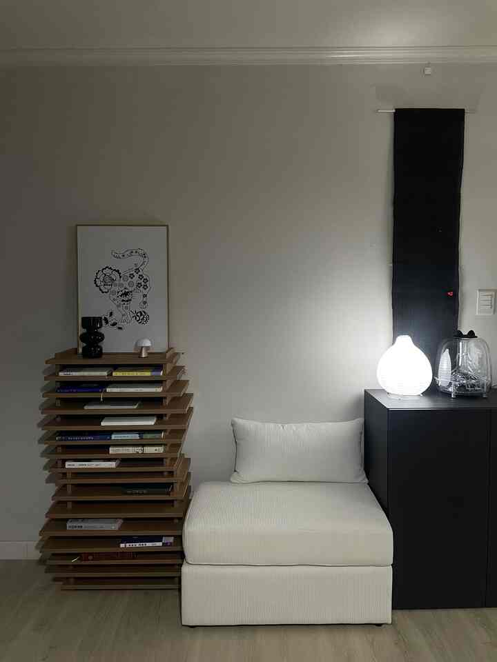 モノトーンのリビング、白いスツールタイプのソファ、木製の本棚、黒いキャビネットが調和したシンプルモダンなインテリア