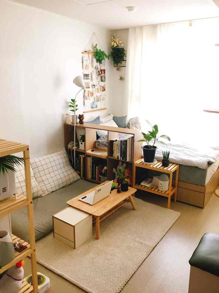 明るいベージュと白のトーンが特徴のワンルーム寝室、木製家具と多様な植物が配置された居心地の良いホームオフィス空間