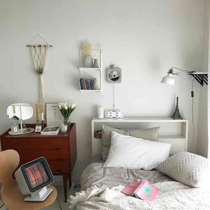 ホワイトトーンの寝室、ベッドと木製チェスト、照明、チューリップの花瓶が配置された温かみのあるインテリア