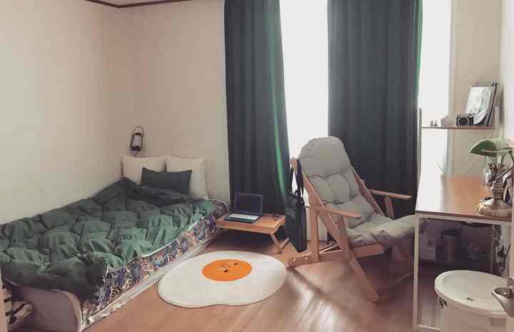 緑色調のコンパクトな寝室、緑の遮光カーテンとベッドが配置された落ち着いた雰囲気のあるインテリア