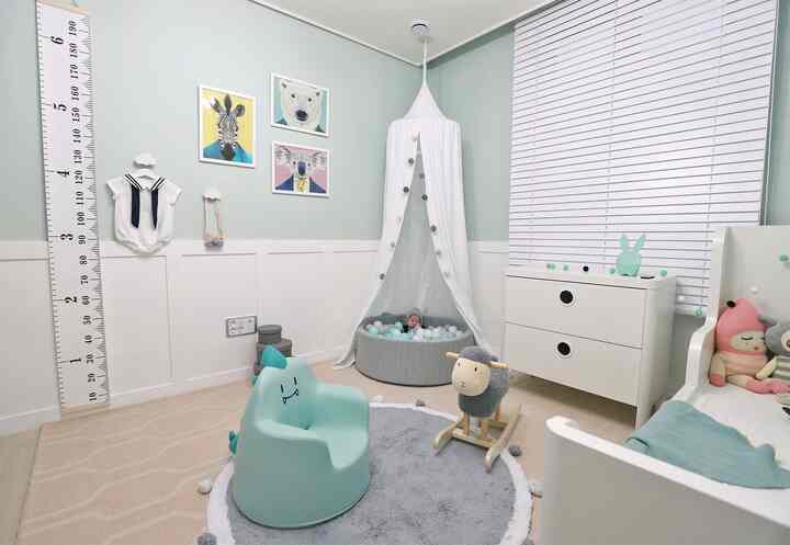 ミントとホワイトの色調の子供部屋、白いキャノピーボールプールとベビーチェア、人形とチェストが配置された雰囲気のある空間