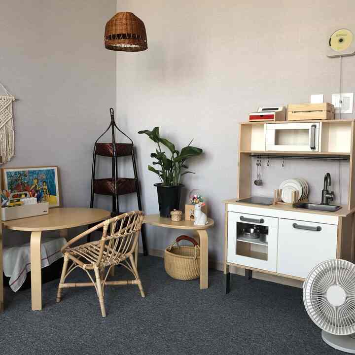 ナチュラルな色調の子供部屋で、ラタンチェア、子供用机、プレイキッチンが配置された雰囲気のあるインテリア