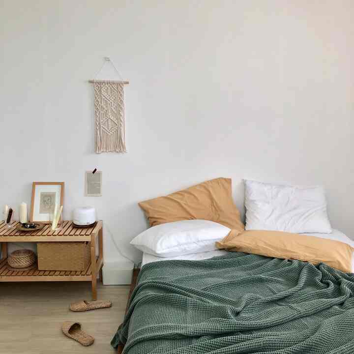 Natural-toned bedroom featuring a beige nightstand and a bed draped with a green blanket, creating a cozy atmosphere