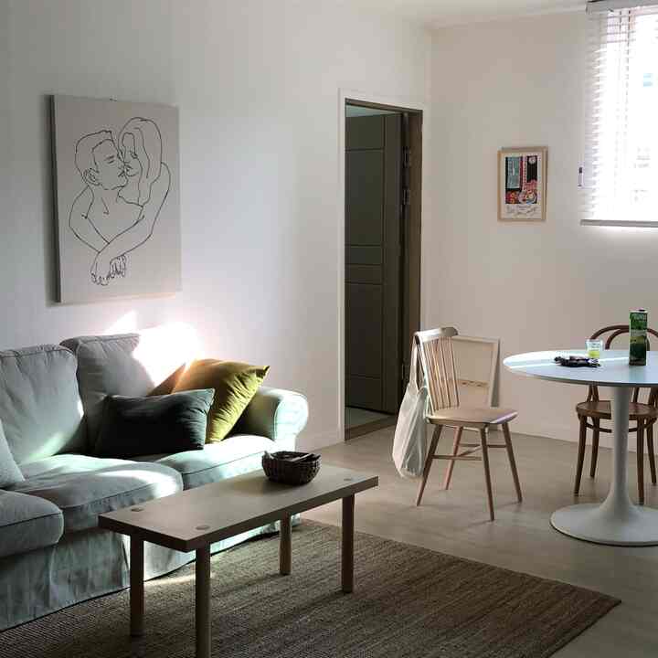 Bright white and wood-toned living room for two featuring natural sofa and dining table in a simple, cozy setting