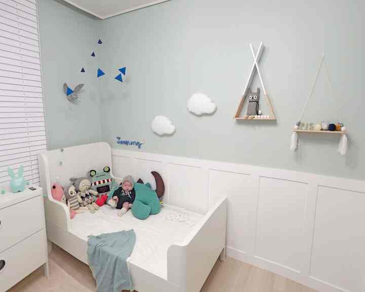 ミント色の壁と白いベッド、赤ちゃんの人形やおもちゃがある印象的なベビールームのインテリア