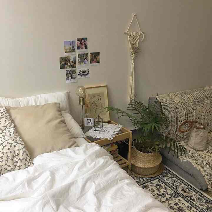 White and beige natural-toned bedroom featuring a bed, nightstand, plant, and textured throws for cozy atmosphere
