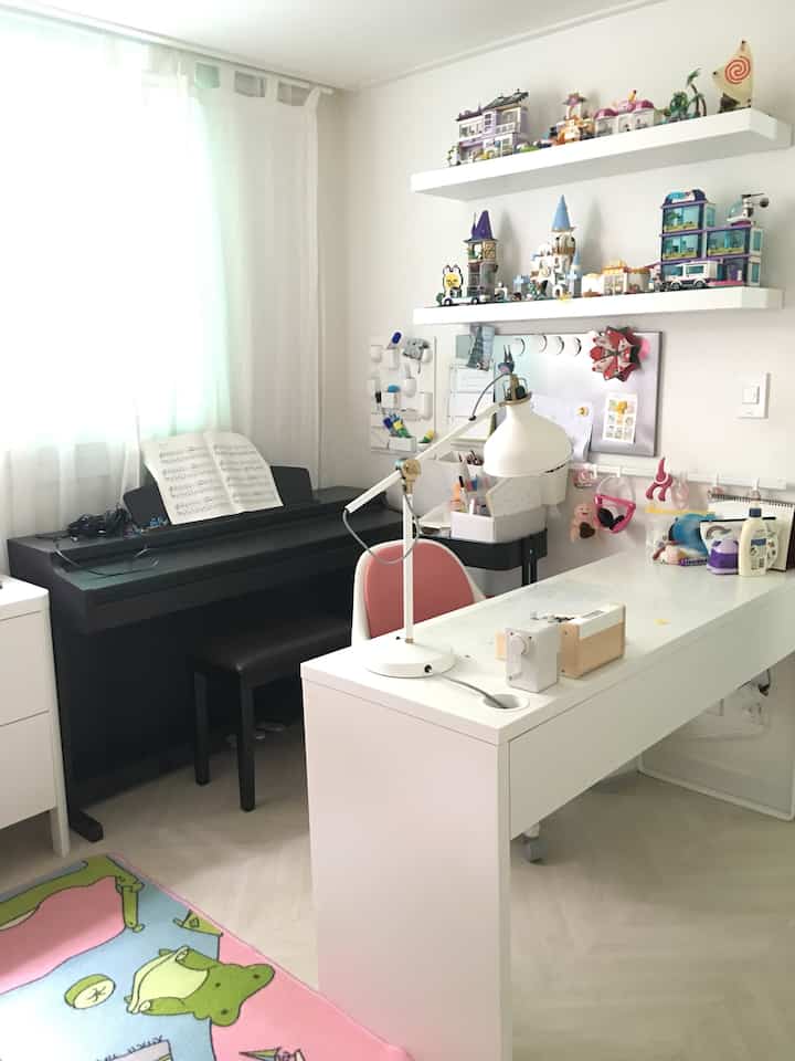 White and natural toned kids' room featuring piano, desk, and toy shelves with tidy atmosphere