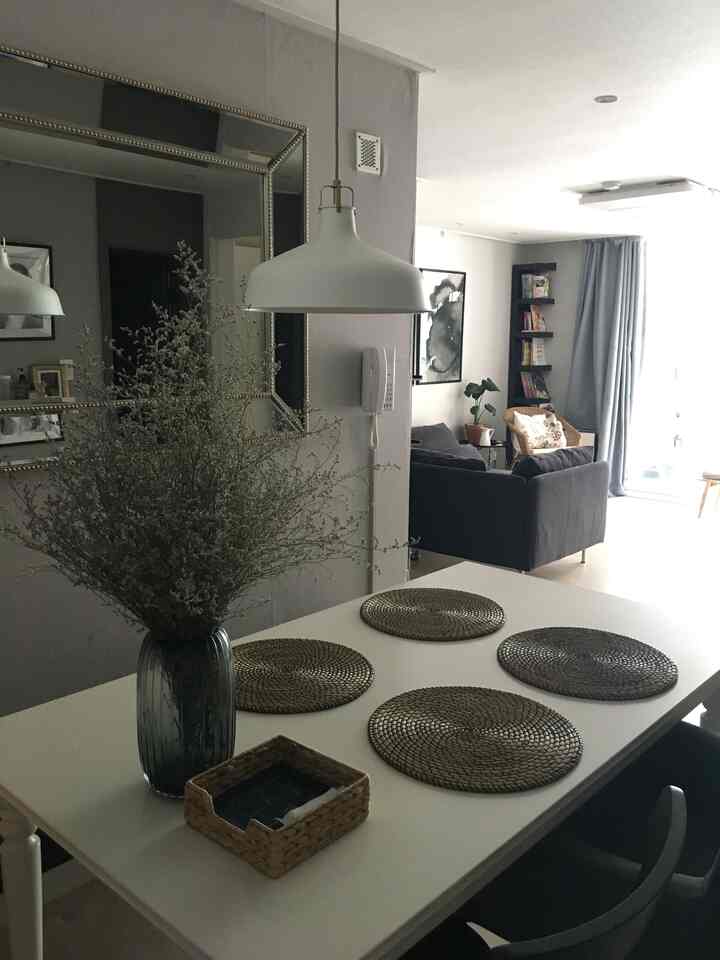 A white and gray-toned living-dining room featuring a central dining table and pendant light with a modern, natural ambiance