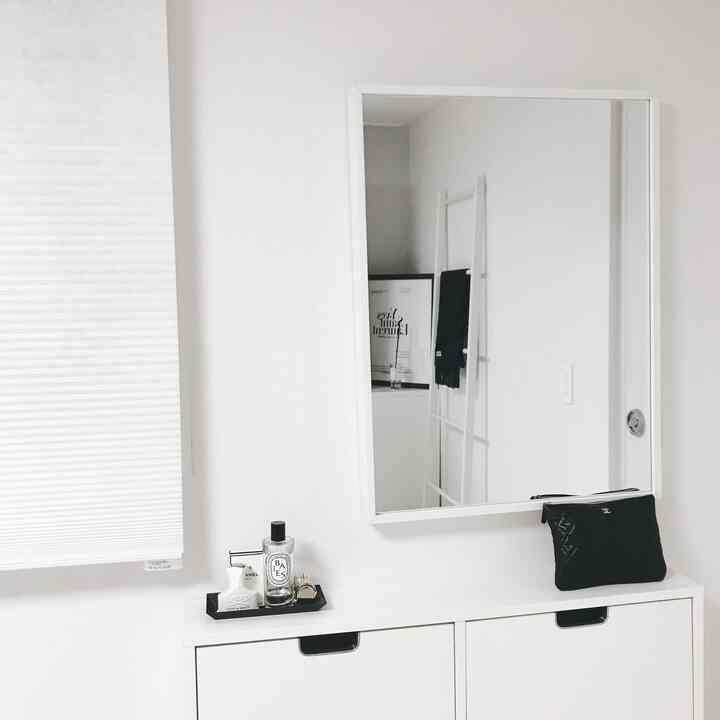 A white-toned bedroom vanity space featuring a clean mirror and pleated blinds with minimalist design