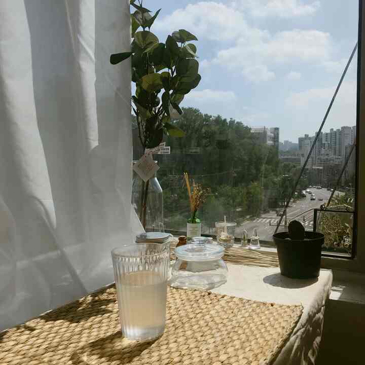 自然光が差し込む窓際のワンルーム、ナチュラルトーンのテーブルマットと透明なグラスが置かれた落ち着いたおうちカフェ風インテリア