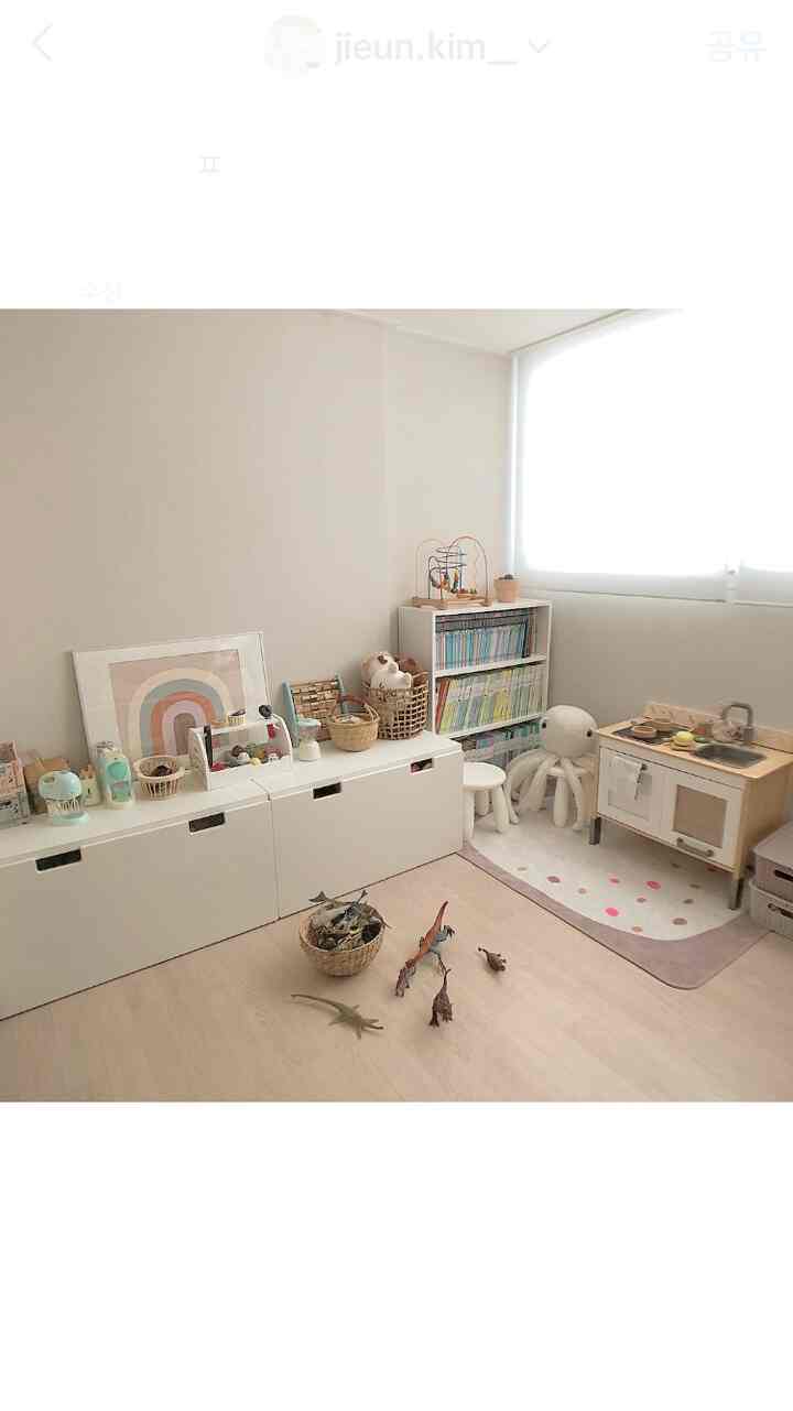 白い壁と木目調の床の子供部屋、低めの収納と子供用キッチン、遊びの本棚が配置された雰囲気のある空間