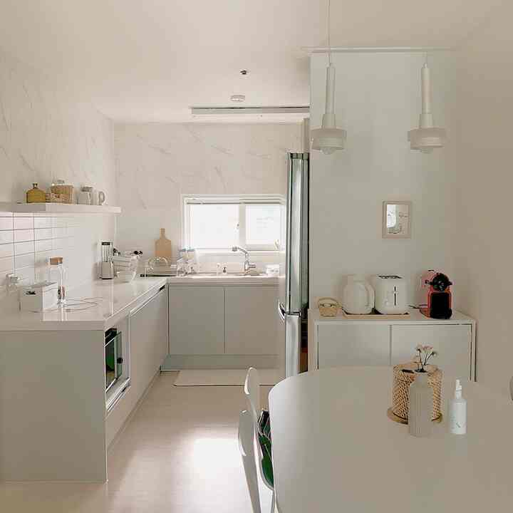 明るいホワイトトーンのキッチン、シンプルなダイニングテーブルとラタンのアクセサリーが配置された清潔感のあるインテリア