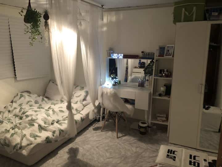 White-toned bedroom featuring a bed with sheer curtains on the left, wardrobe and vanity desk on the right, creating a cozy atmosphere