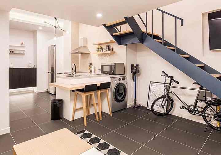 A modern Nordic style loft living and kitchen area in white and dark gray tones, featuring a kitchen island and staircase in a long rectangular room