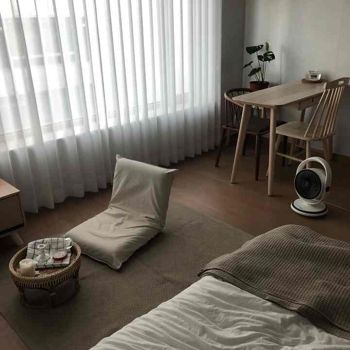 Natural color and white toned studio living and bedroom space featuring wooden furniture and soft textiles with a cozy atmosphere