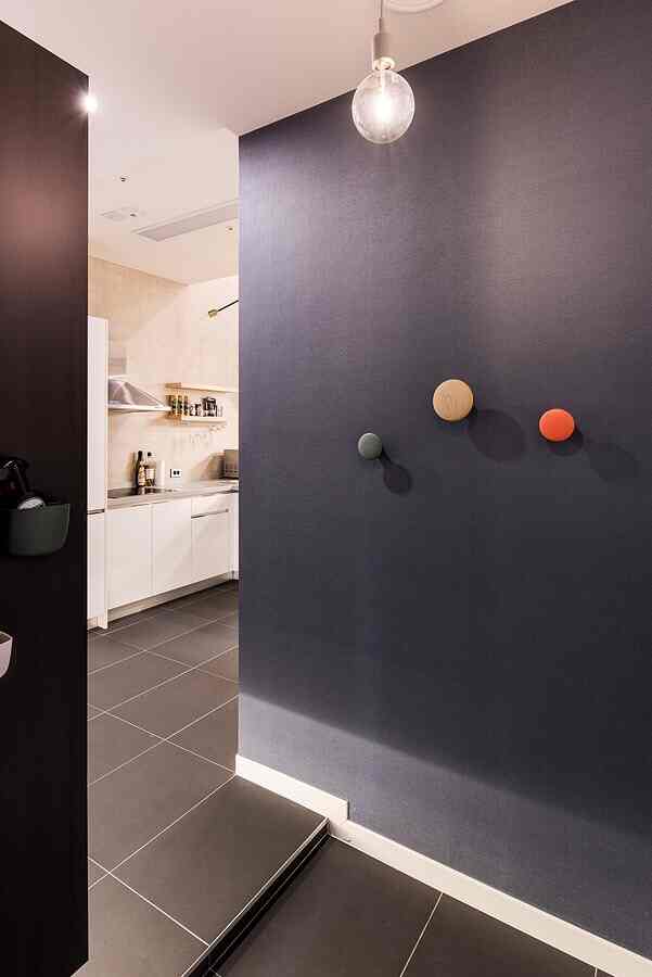 Entrance with dark gray wall and gray tiled floor, wooden and colorful hooks, simple pendant light creating a clean look