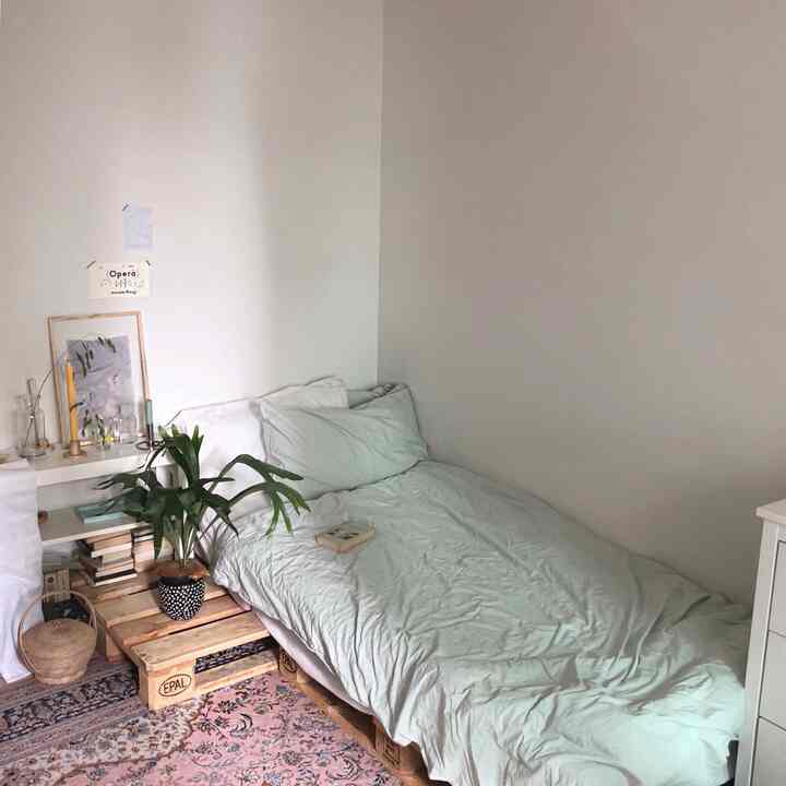 Mint-toned bedding in a studio apartment bedroom featuring wooden pallet table and green plant, creating a natural and simple atmosphere