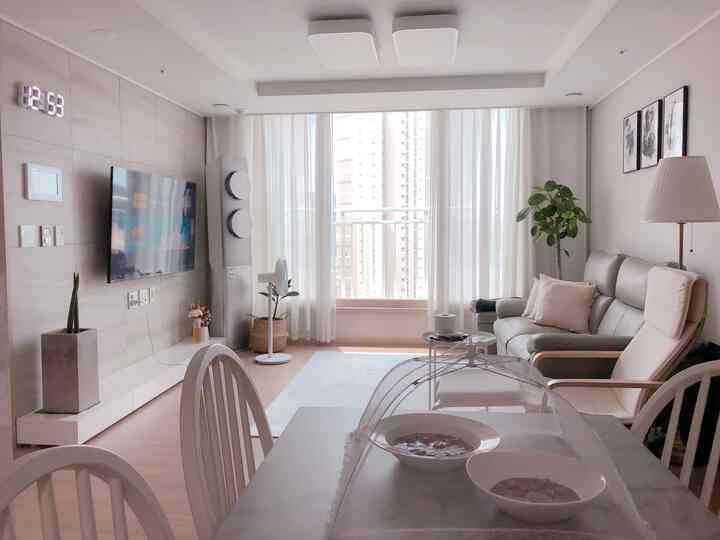 A bright 25-pyeong apartment living and dining room in white and gray tones featuring modern sofa and armchair with large window and curtains