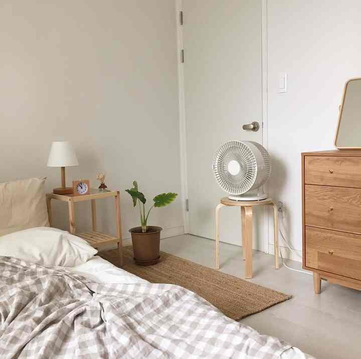 ベージュトーンの寝室、木製のチェストとナイトテーブル、植物が配置された落ち着いたナチュラルモダンなインテリア