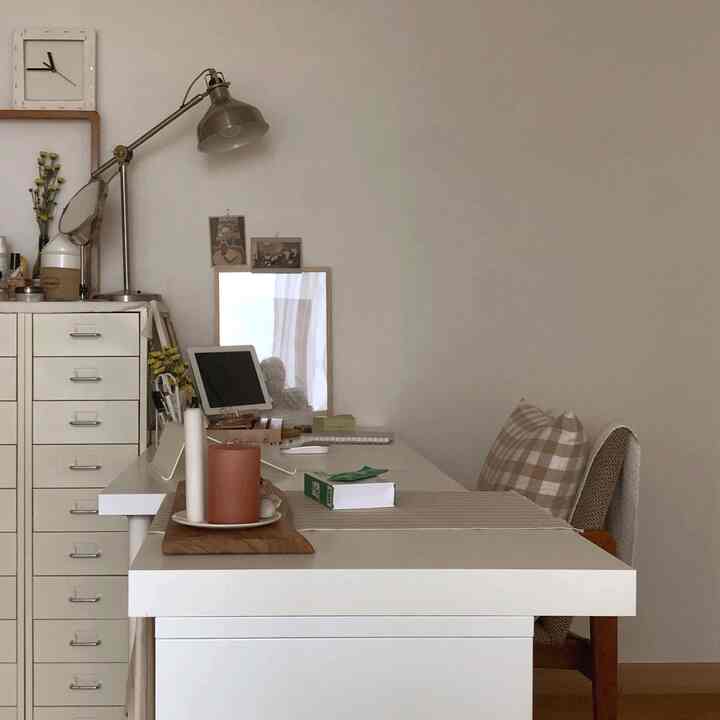 White-toned home office space featuring a neatly arranged dresser and desk with cozy candle lighting